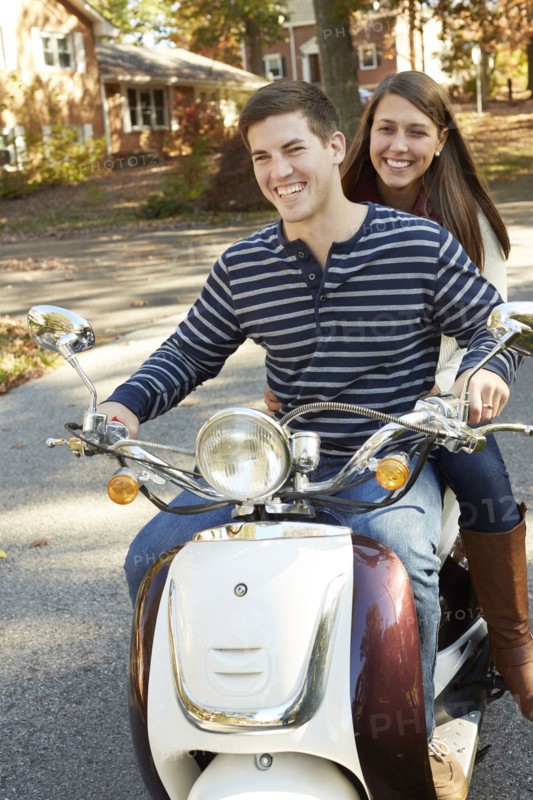 Couple riding scooter in suburban neighborhood