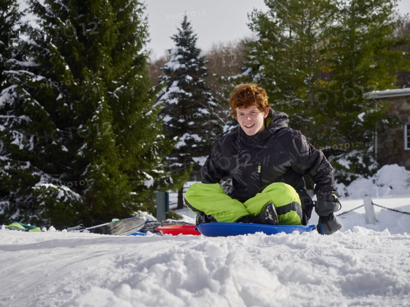 Caucasian teenage boy sledding on snowy hill