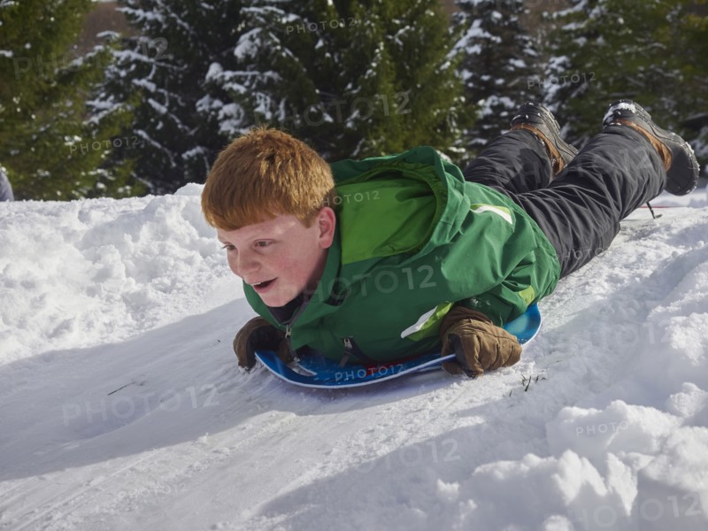 Caucasian boy sledding on snowy hill