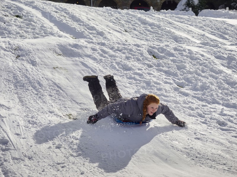 Caucasian teenage girl sledding on snowy hill