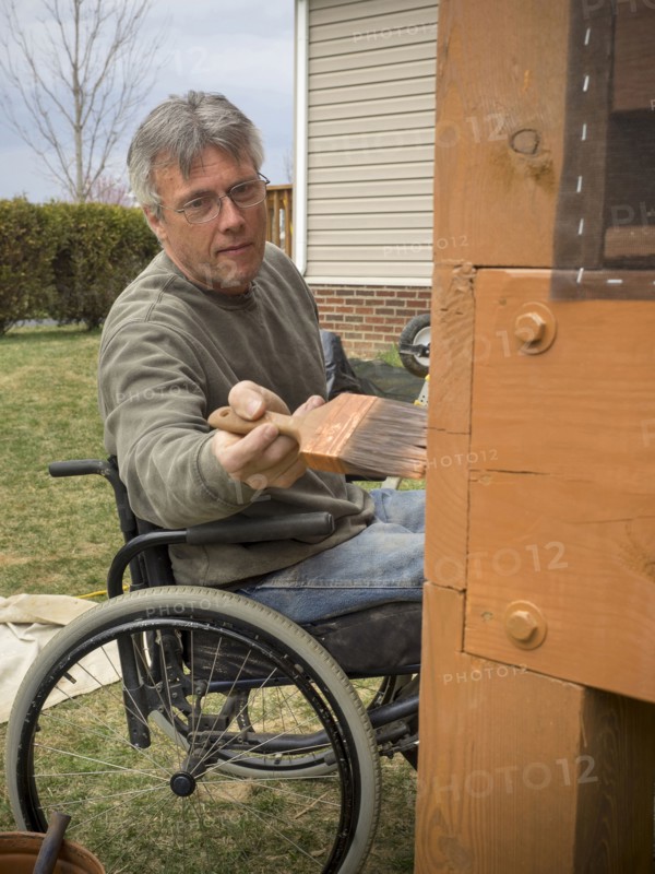 Caucasian paraplegic man painting deck in backyard