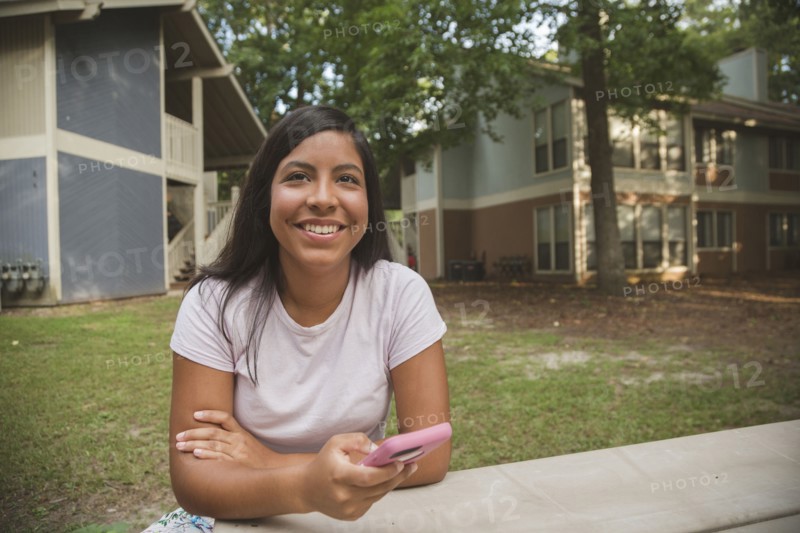 Smiling Hispanic girl holding cell phone near apartments