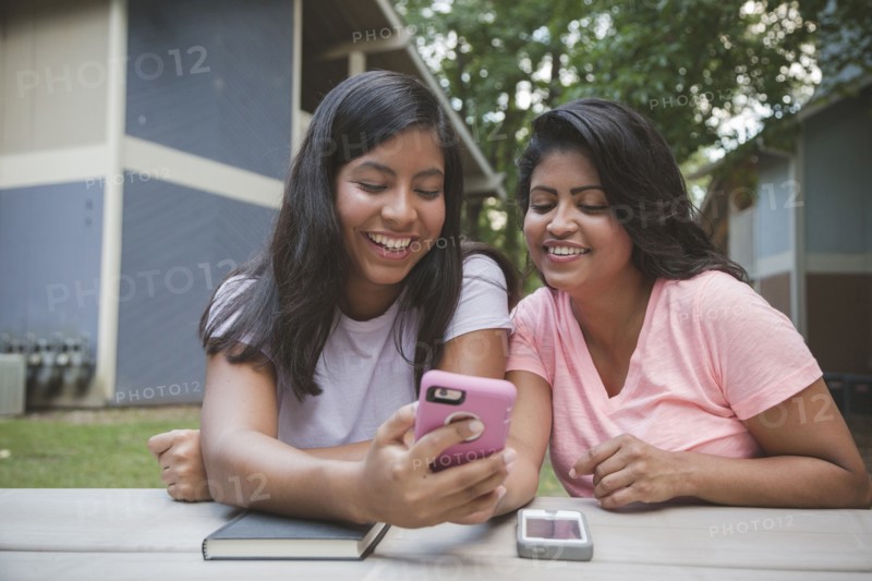 Hispanic mother and daughter texting on cell phone near apartments