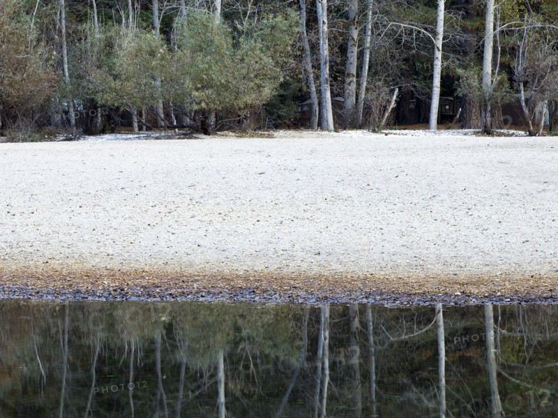 Trees and sandy beach reflecting in still river