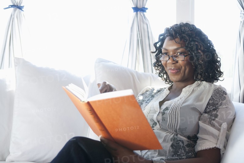 Black woman reading book on sofa