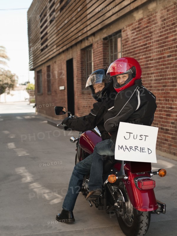 Caucasian couple riding on motorcycle with Just Married sign