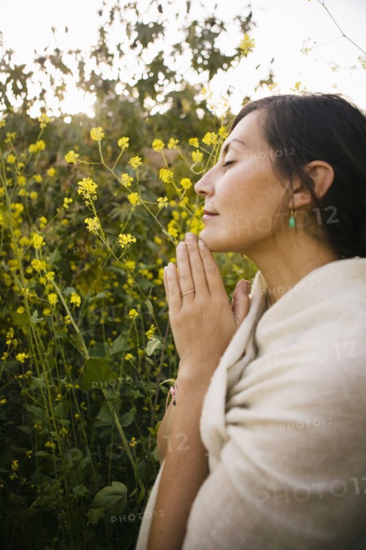 Mixed race woman praying with eyes closed in field