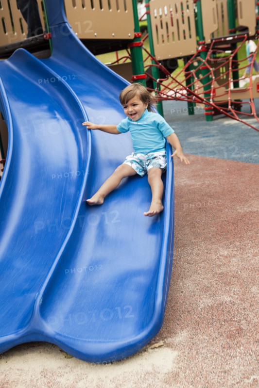 Mixed race boy sliding down slide in playground