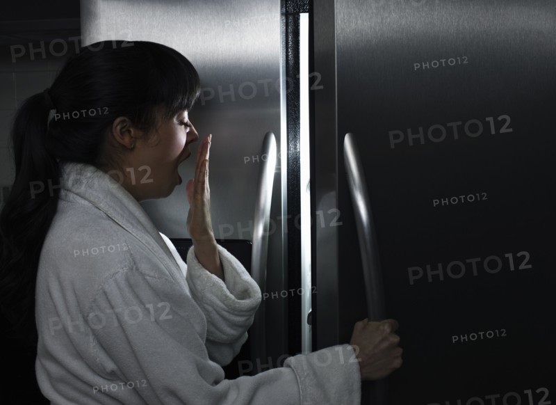 Sleepy mixed race woman looking in refrigerator at night