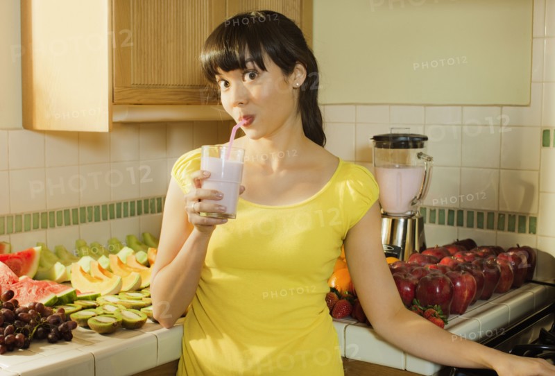 Mixed race woman drinking smoothie in kitchen