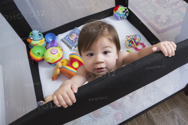 Mixed race baby girl standing in playpen