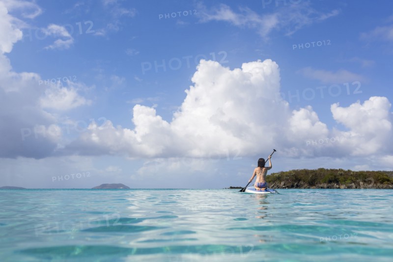 Caucasian woman paddling surfboard on tropical ocean