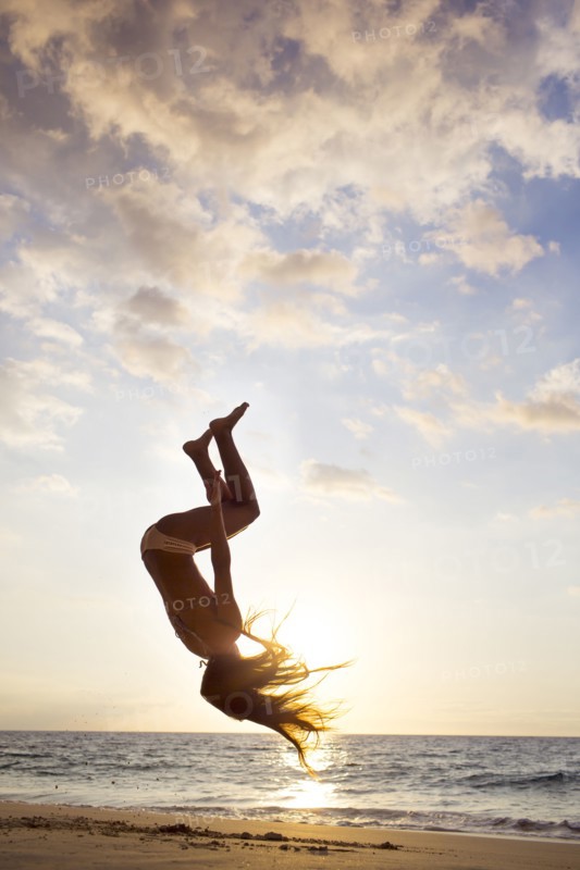Silhouette of mixed race woman doing backflip on beach