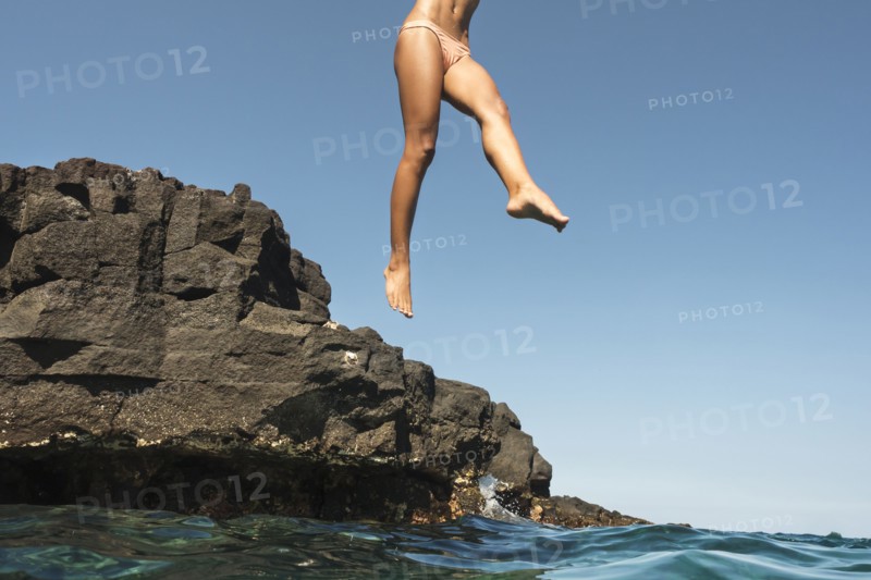 Mixed race woman jumping from rocks into ocean