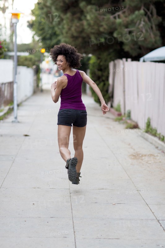 Smiling Mixed Race woman running on sidewalk