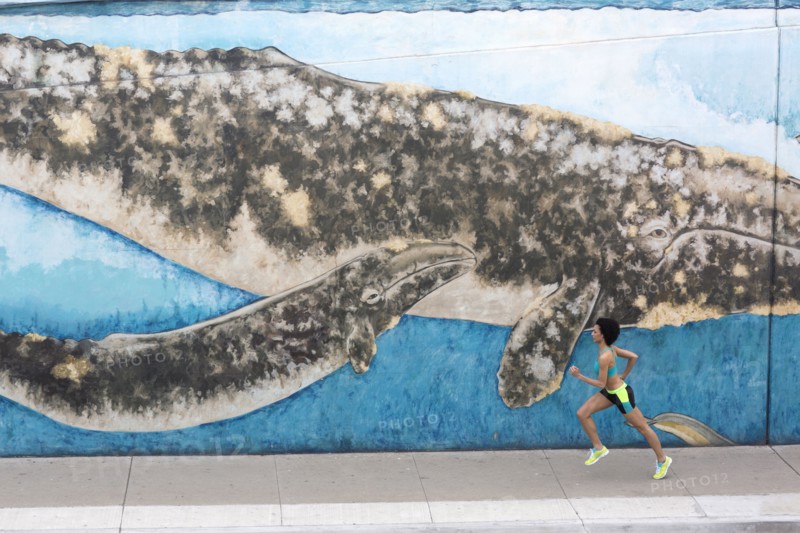 Distant Mixed Race woman running on sidewalk near mural
