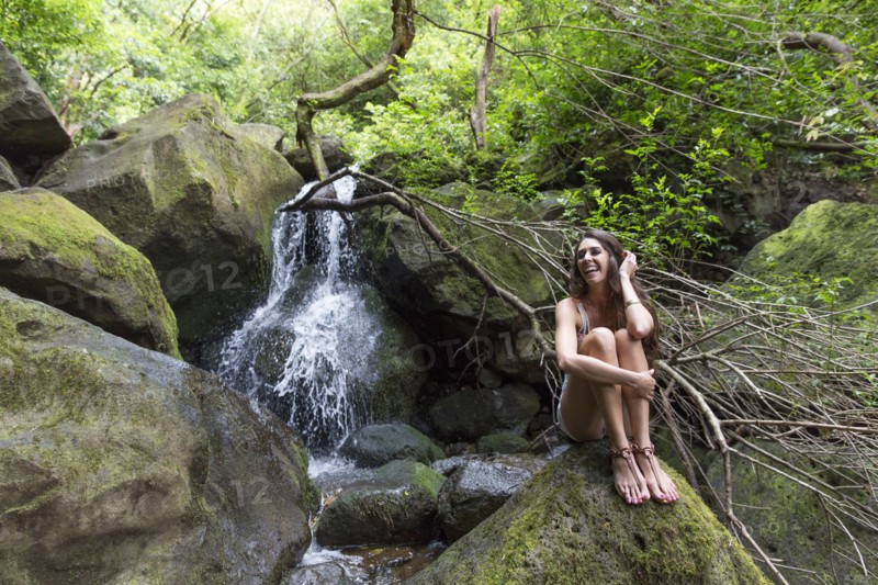 Mixed Race woman sitting on rock near waterfall