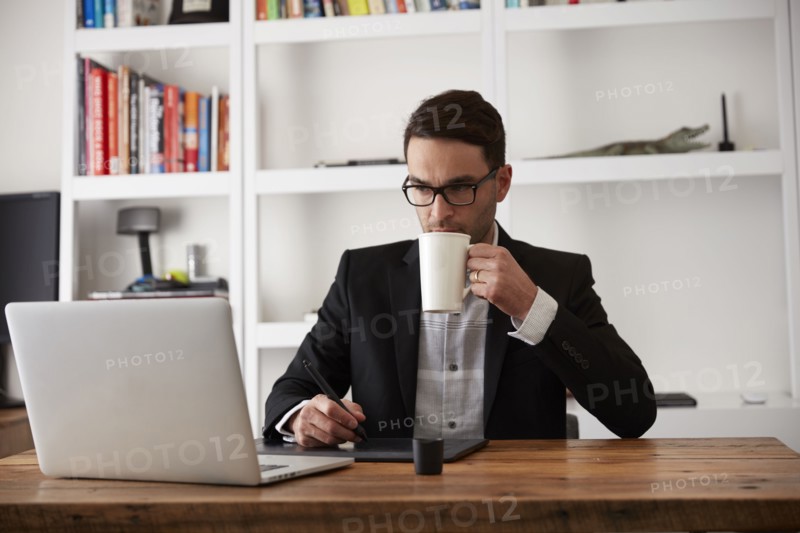 Caucasian businessman using laptop and digital tablet drinking coffee