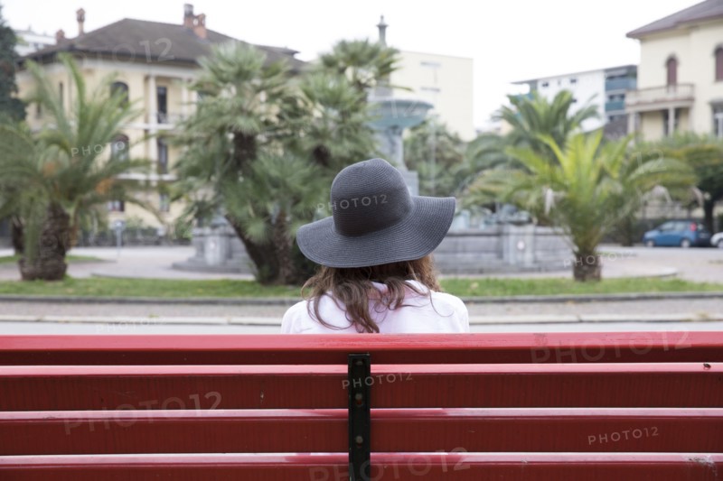 Woman wearing sun hat sitting on red bench