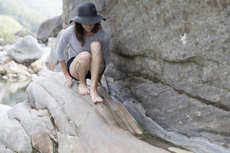 Woman wearing sun hat crouching on rock
