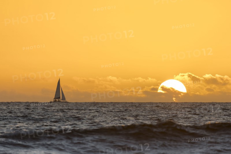 Distant sailboat in ocean at sunset