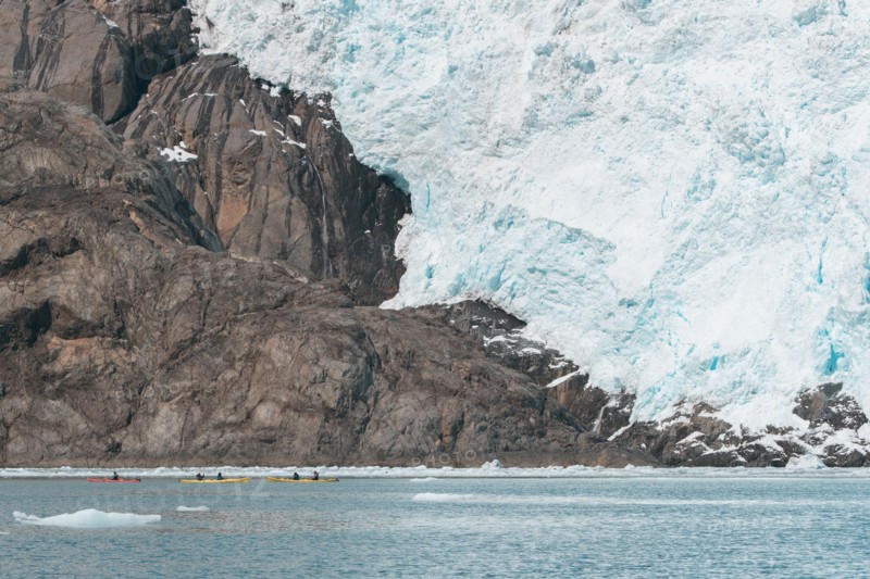 Distant people kayaking near glacier