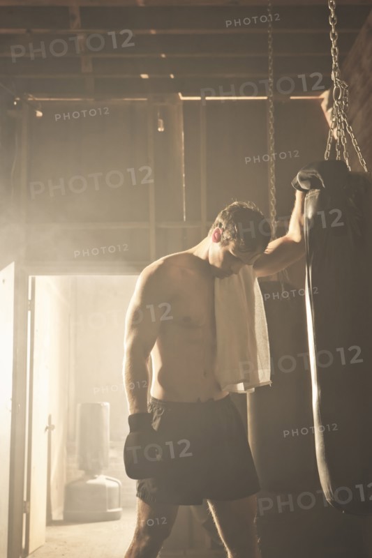Fatigued boxer leaning on punching bag