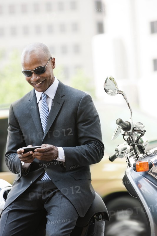 Black businessman sitting on scooter text messaging