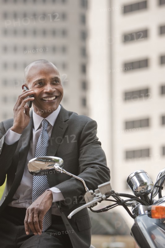 Black businessman sitting on scooter talking on cell phone