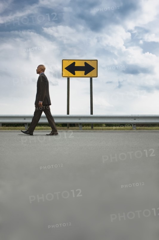 African American businessman walking on road near road sign