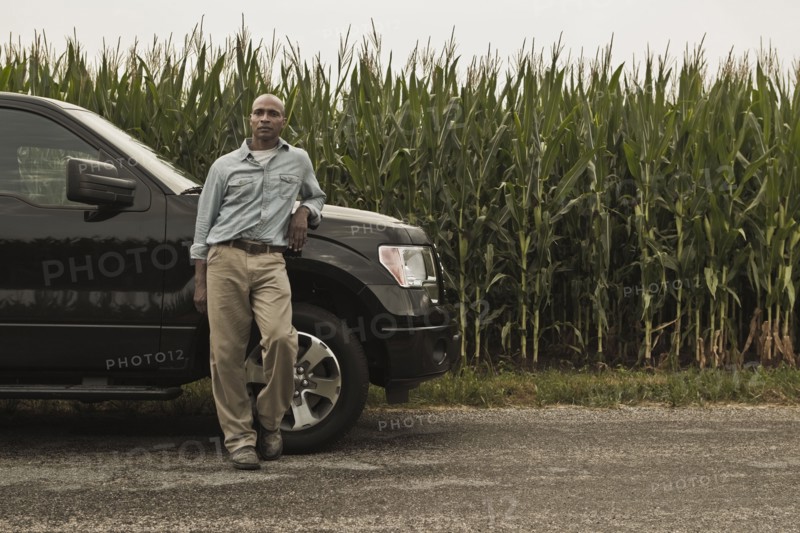 African American farmer leaning on car next to crop