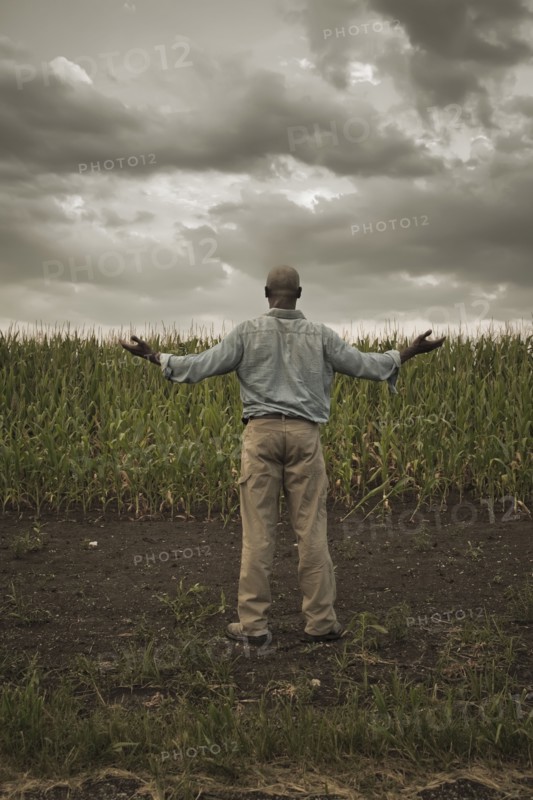 African American farmer standing in field with arms outstretched
