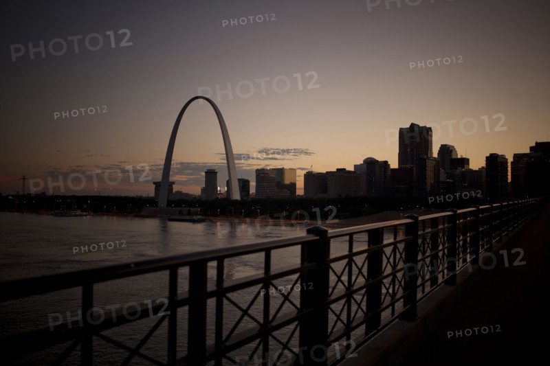 Arch landmark next to urban river at sunset