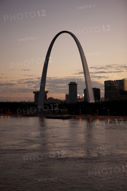 Arch landmark next to urban river at sunset