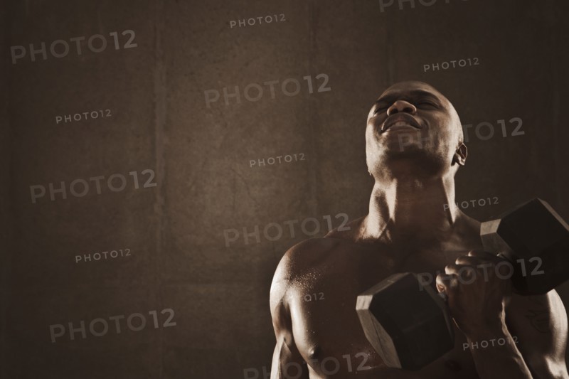 Grimacing African American man lifting weights