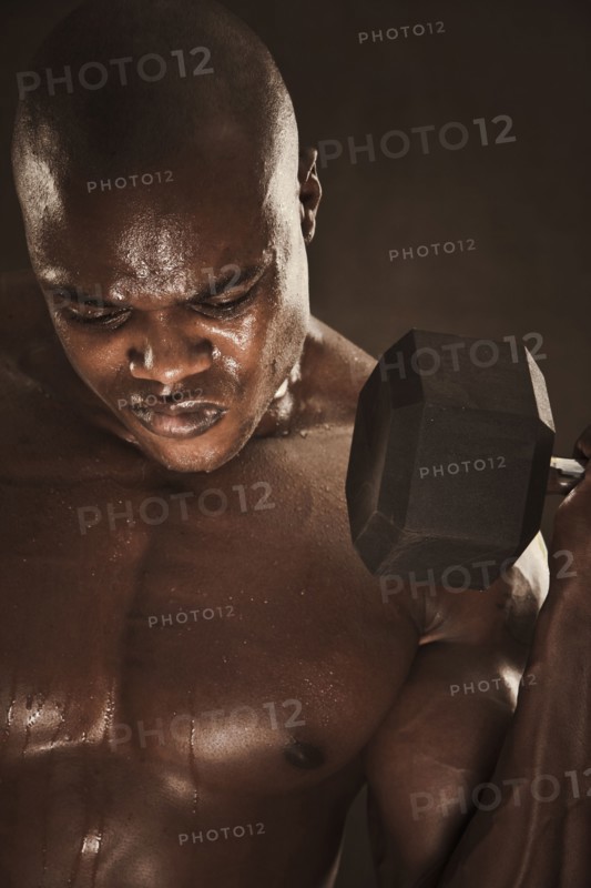 Grimacing African American man lifting weights
