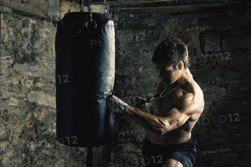 Caucasian boxer training and hitting punching bag