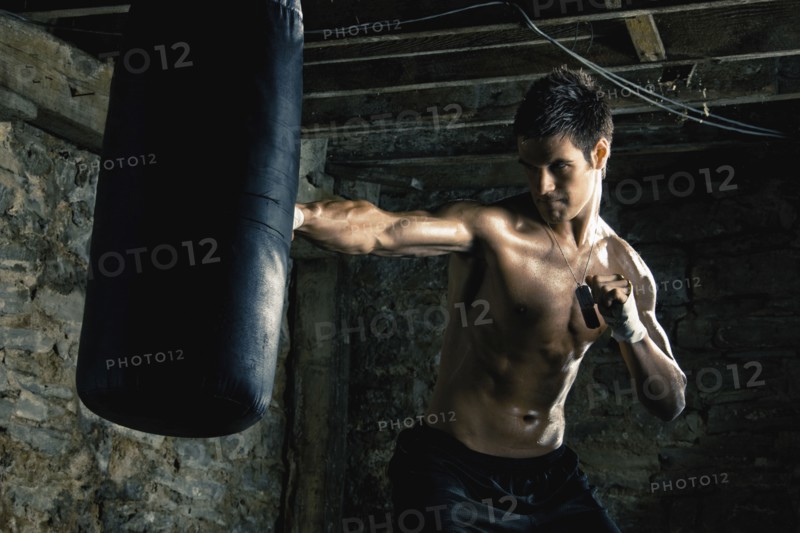 Caucasian boxer training and hitting punching bag