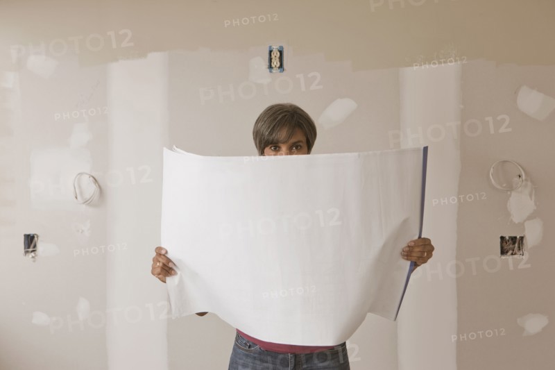 Mixed race woman standing in unfinished room with blueprints