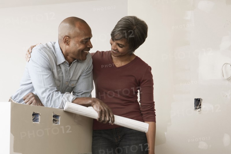 Couple standing in unfinished room with blueprints