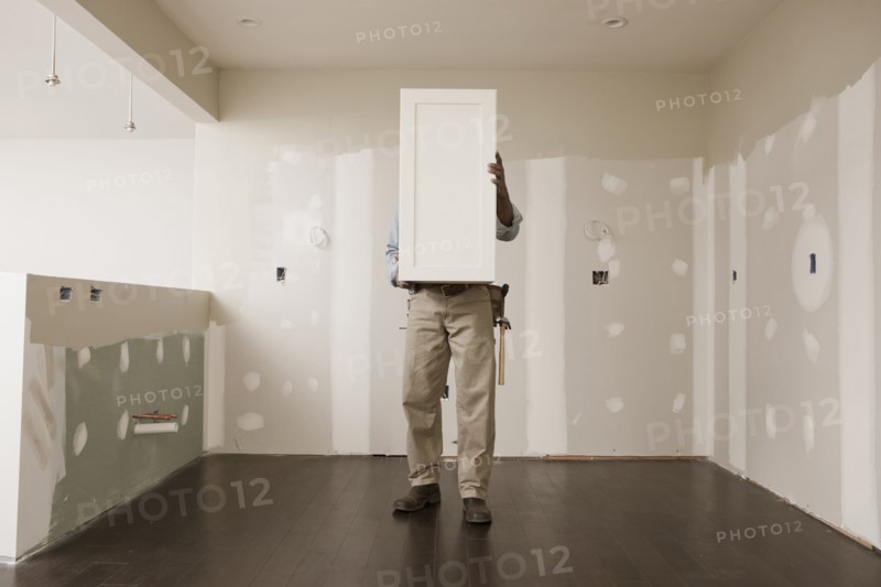 African American man holding cabinet door in unfinished room