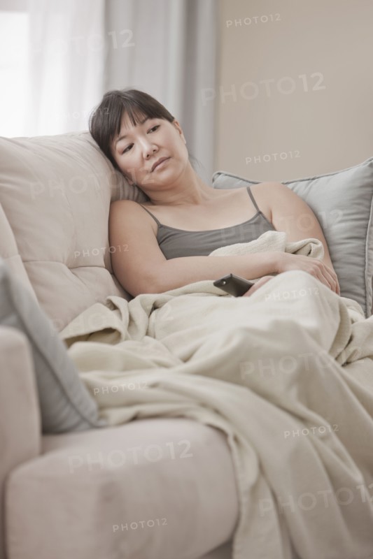Asian woman laying on sofa watching television