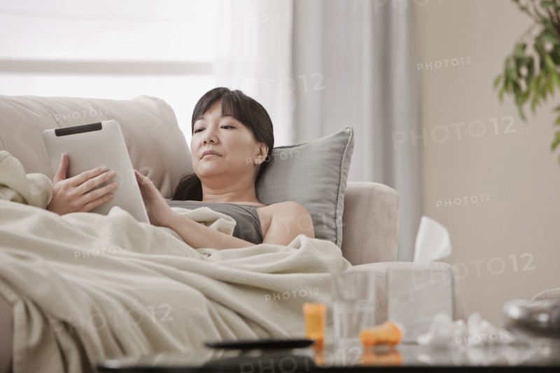 Sick Asian woman using digital tablet on sofa