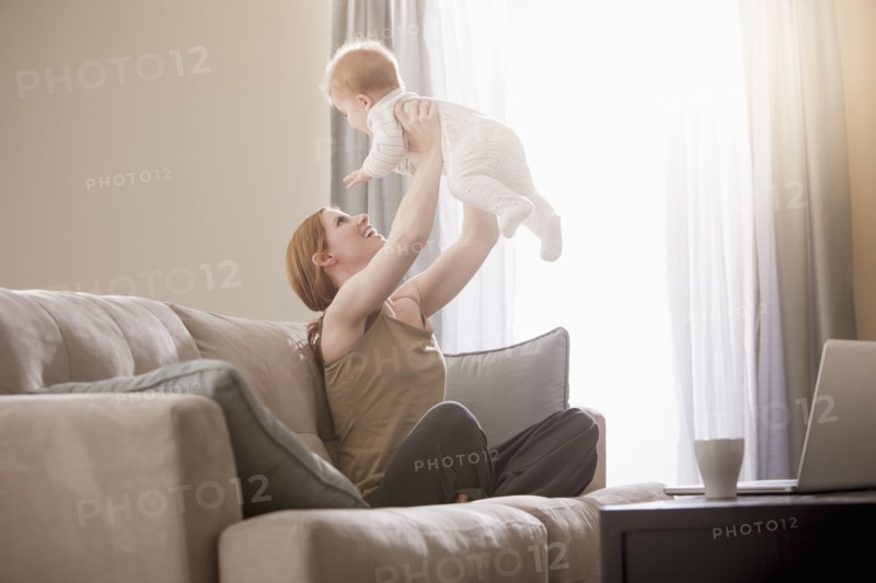 Caucasian mother on sofa lifting son