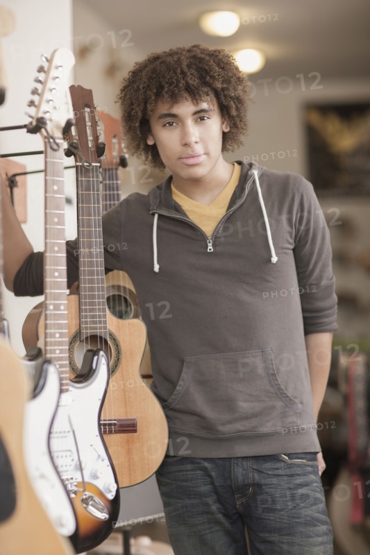 Mixed race teenager standing with guitars in music store