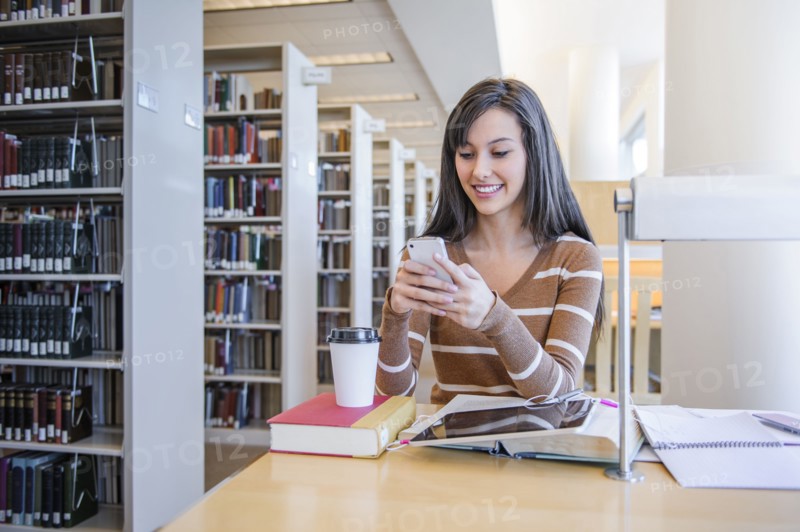 Student using cell phone at desk in library