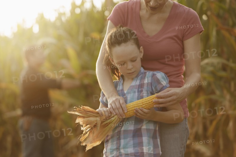 Caucasian mother and daughter examining ear of corn