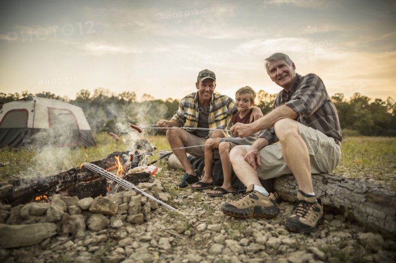 Three generations of Caucasian men roasting hot dogs over campfire