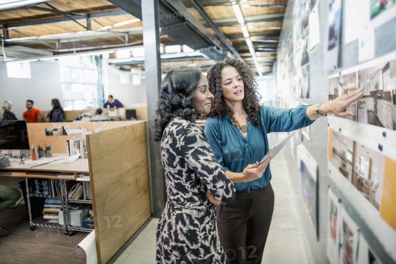 Businesswomen examining photographs on wall in office