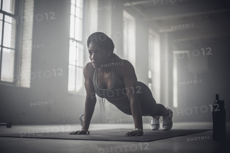 Black woman doing push-ups in dark gym